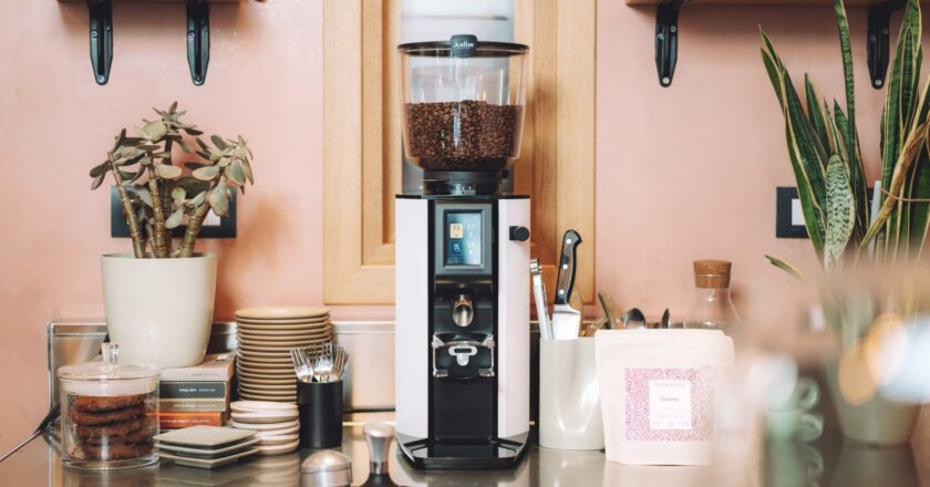 Coffee grinder on a kitchen counter with pink walls and decorative elements.